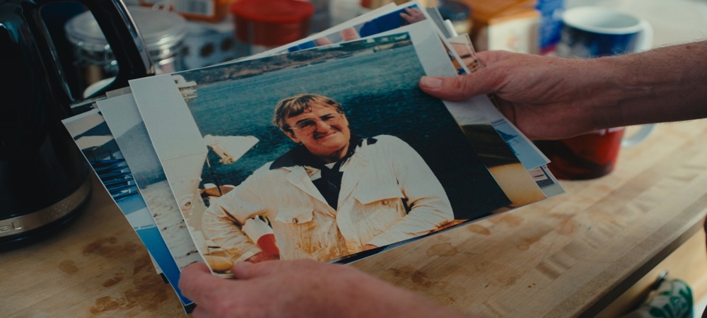 Hands holding a collection of printed photographs on a kitchen table, with a portrait photo on top. 