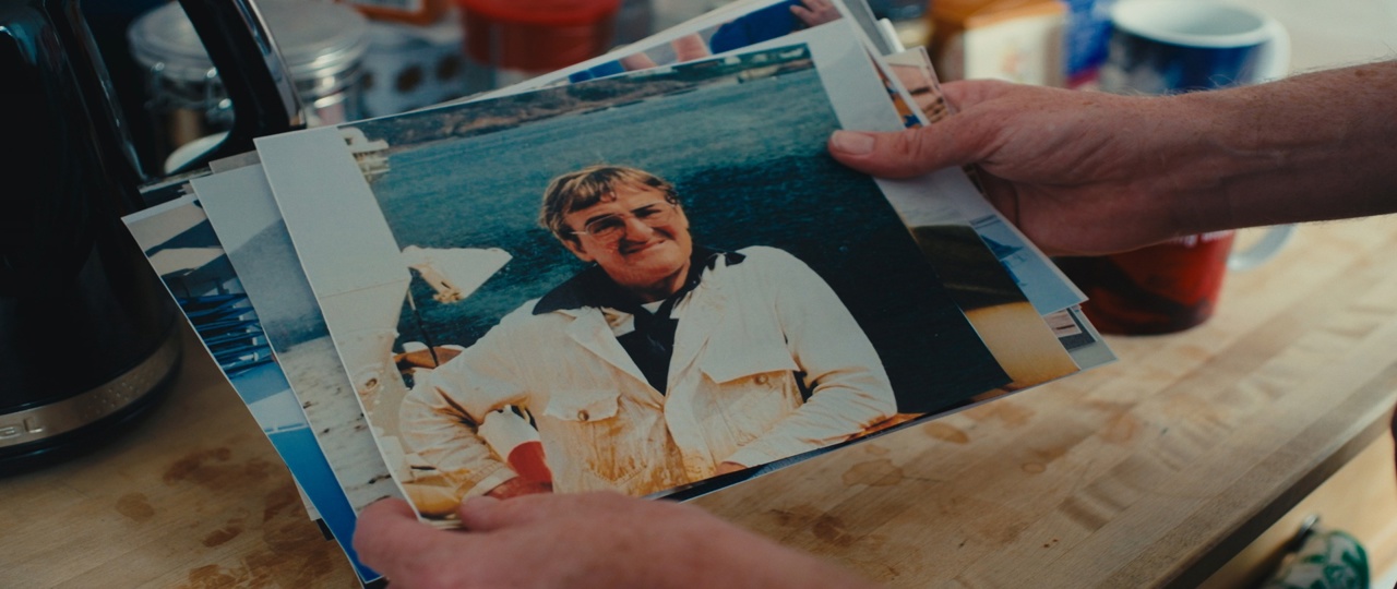 Hands holding a collection of printed photographs on a kitchen table, with a portrait photo on top. 