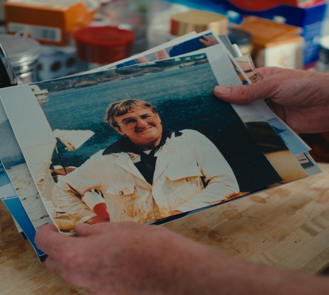 Hands holding a collection of printed photographs on a kitchen table, with a portrait photo on top. 