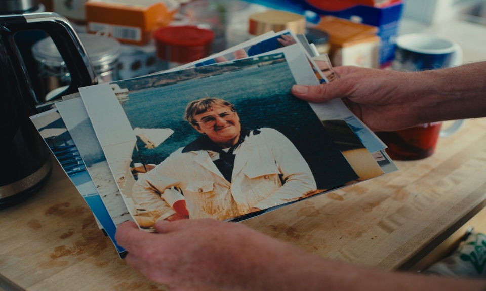 Hands holding a collection of printed photographs on a kitchen table, with a portrait photo on top. 