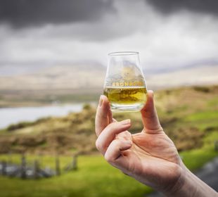 A glass of whisky being held aloft outdoors