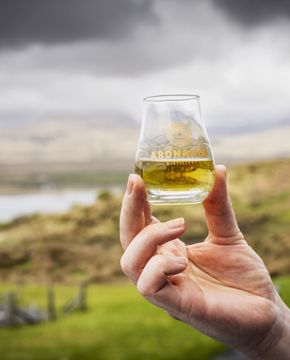 A glass of whisky being held aloft outdoors