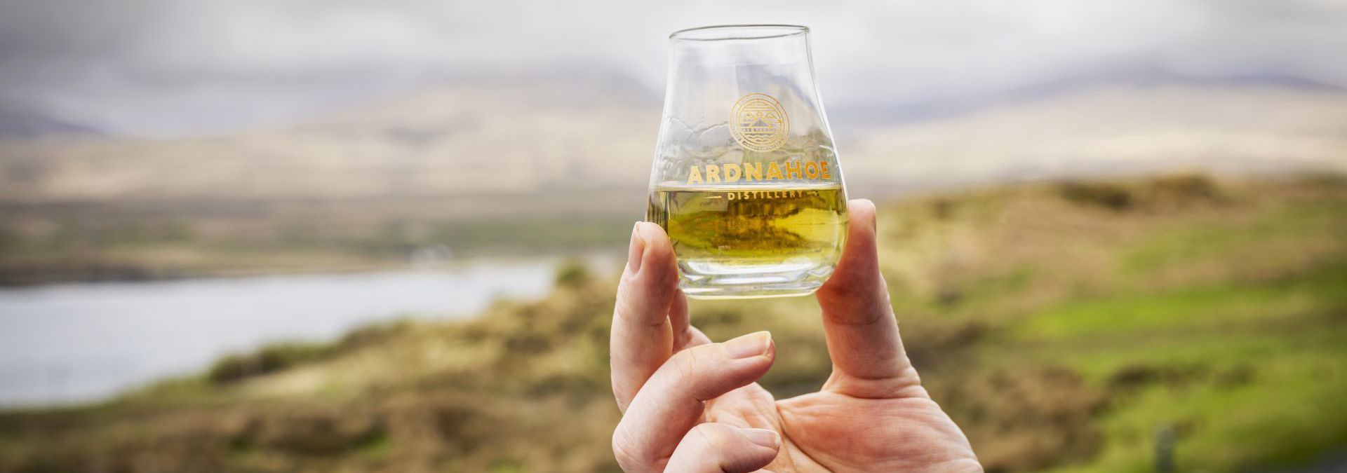 A glass of whisky being held aloft outdoors