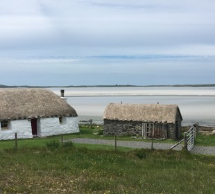 White thatched cottage and stone hut near a calm beach under a cloudy sky.