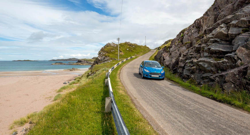 Car driving on single track island road next to a coastal view.