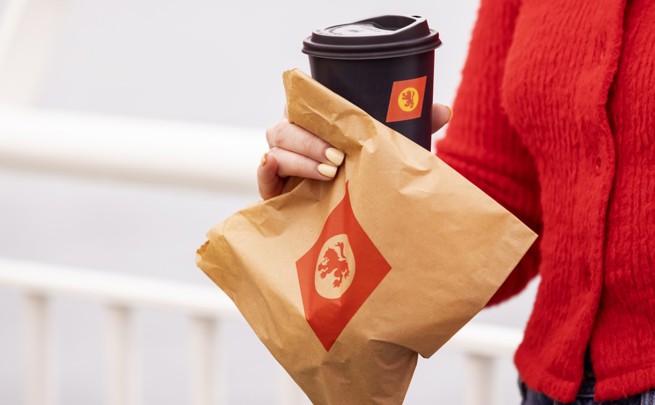 girl in a red sweater holding a brown paper bag with CalMac logo and a cup of coffee in  a black cup