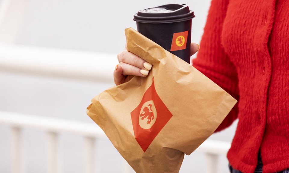 girl in a red sweater holding a brown paper bag with CalMac logo and a cup of coffee in  a black cup