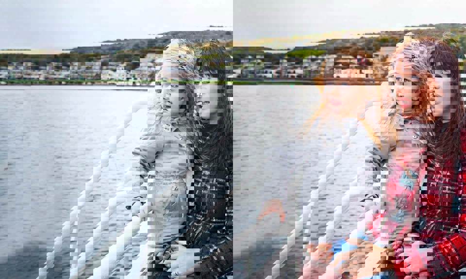 Mother with daughter in her arms looking out to the sea from the outside deck of a ferry