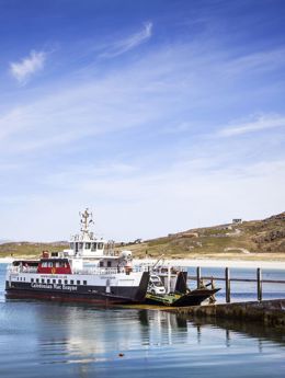 CalMac Ferry at slipway, with a beach and hill landscap behind, under a blue sky. Eriskay ferry.