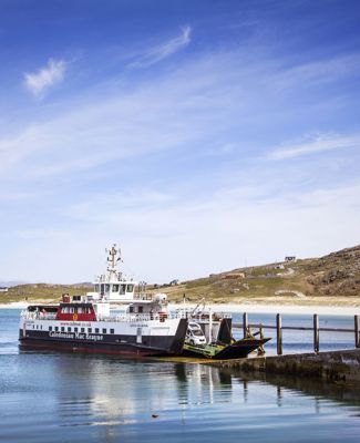 CalMac Ferry at slipway, with a beach and hill landscap behind, under a blue sky. Eriskay ferry.