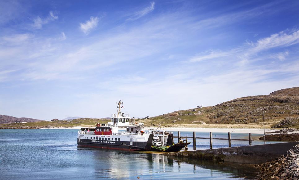 CalMac Ferry at slipway, with a beach and hill landscap behind, under a blue sky. Eriskay ferry.