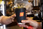 person handing over a black CalMac branded compostible cup to another person. 