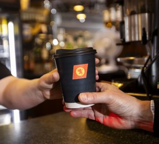 person handing over a black CalMac branded compostible cup to another person. 