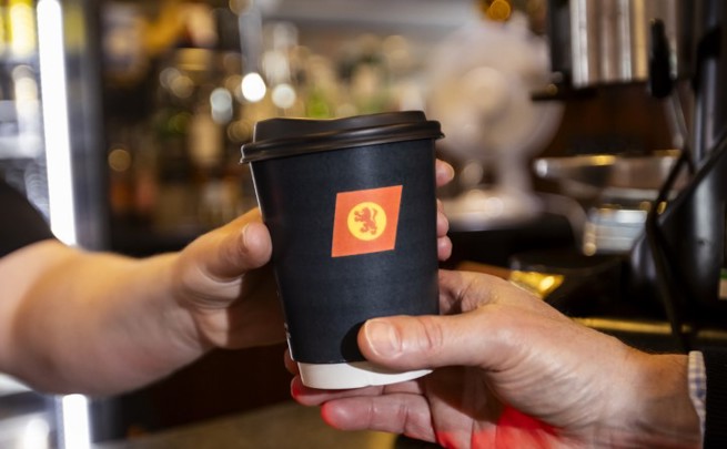 person handing over a black CalMac branded compostible cup to another person. 