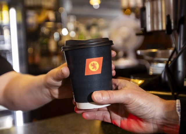 person handing over a black CalMac branded compostible cup to another person. 