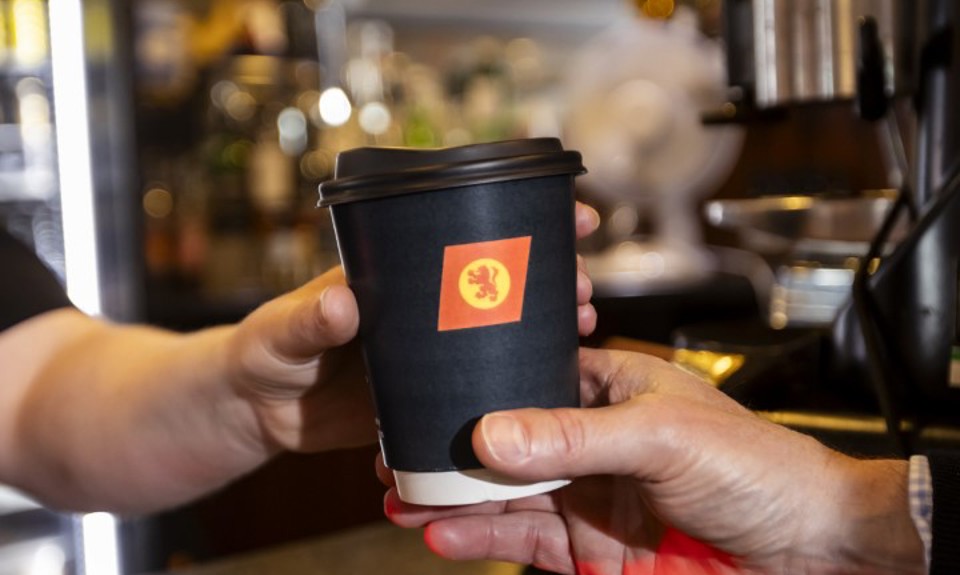 person handing over a black CalMac branded compostible cup to another person. 